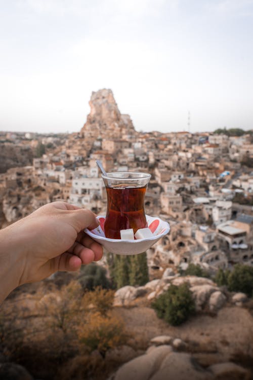 Hand Holding Glass of Tea over Town in Cappadocia