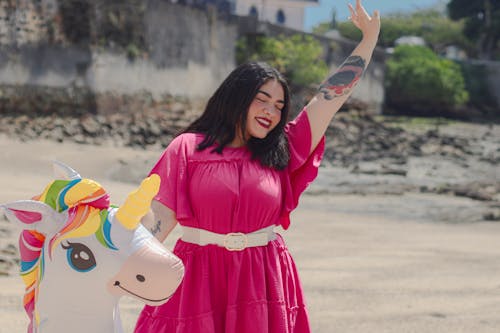 A woman in a pink dress and unicorn toy on the beach