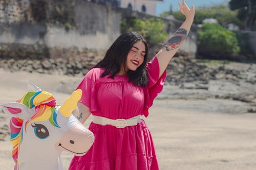 Brunette Woman in Pink Dress Standing with Arm Raised and Balloon Unicorn