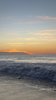 Peaceful sunset over the sea with waves crashing on the shoreline.