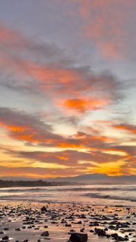 A stunning coastal sunrise with vivid clouds over a tranquil beach and sea.