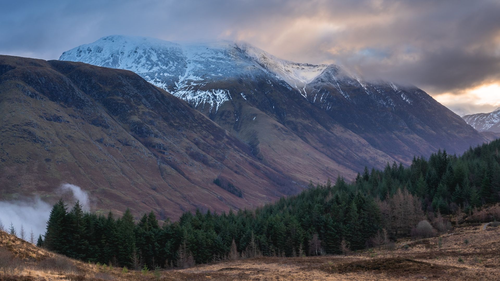 Capture the serene landscape of Ben Nevis with snow-capped peaks and lush forests at dawn in Fort William, Scotland.