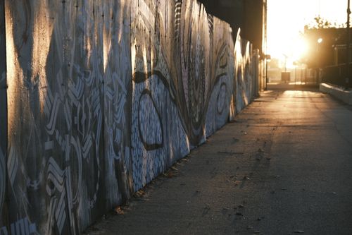 Free A city street showcasing vibrant graffiti artwork illuminated by the soft light of sunrise. Stock Photo