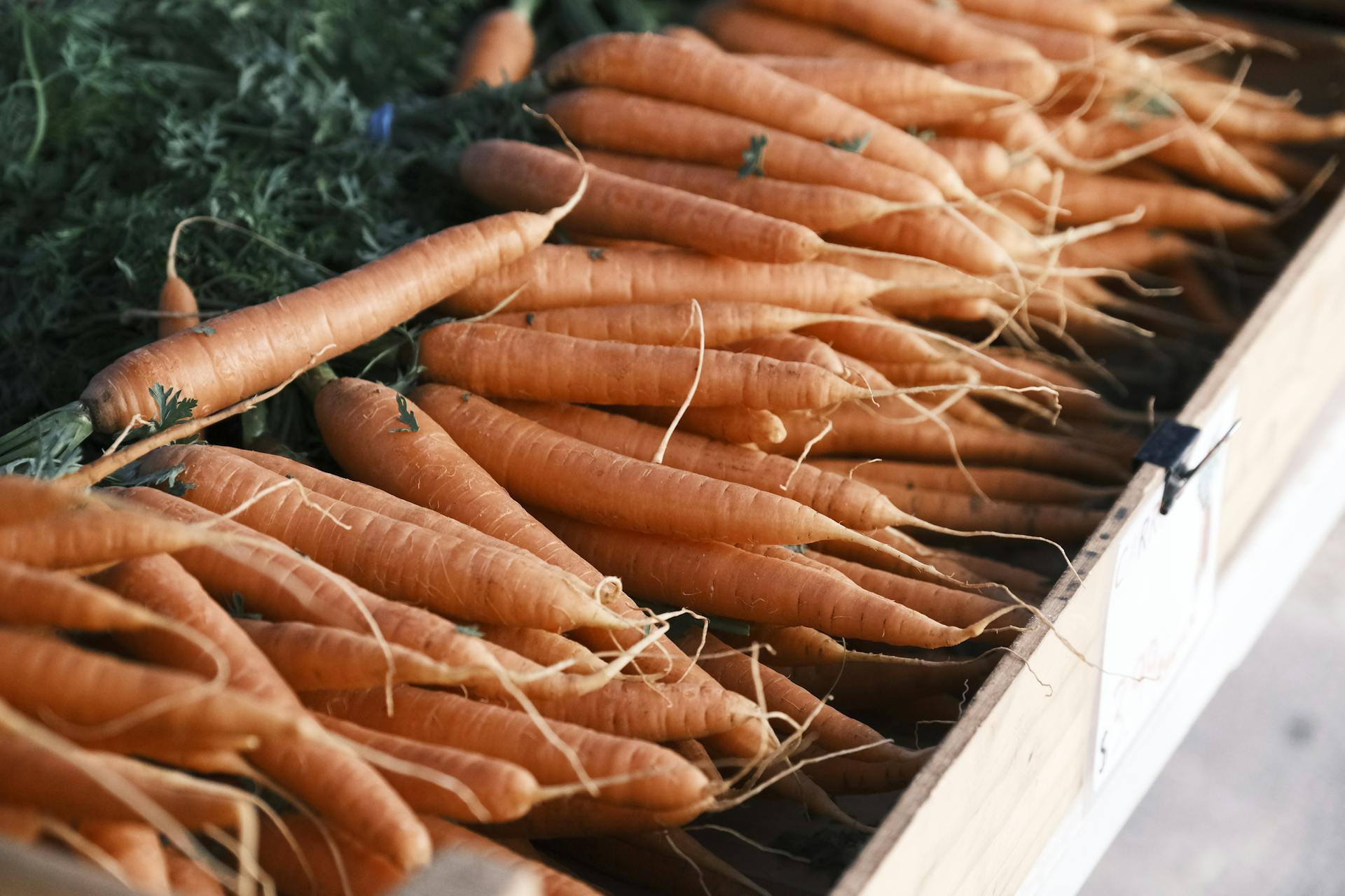 A close-up of fresh organic carrots on display at a farmer's market wooden stall, ready for purchase.