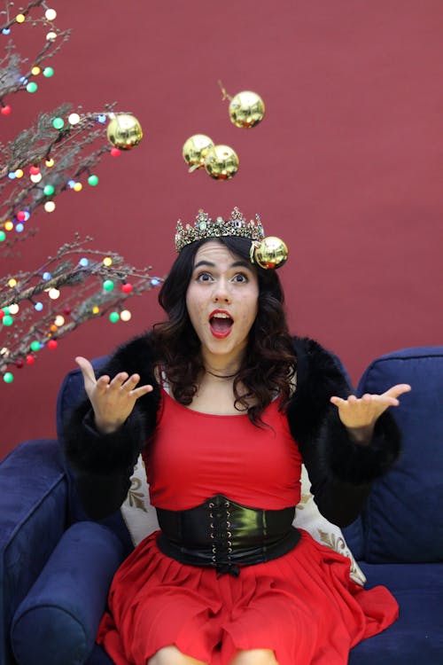 A woman in a red dress and crown is juggling balls