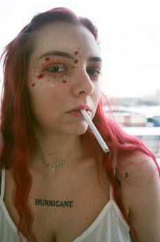 一位红发女子化着闪光妆，手持香烟摆出姿势，展现出大胆而艺术的造型