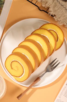 Sliced Swiss roll cake on white plate with fork in warm lighting.