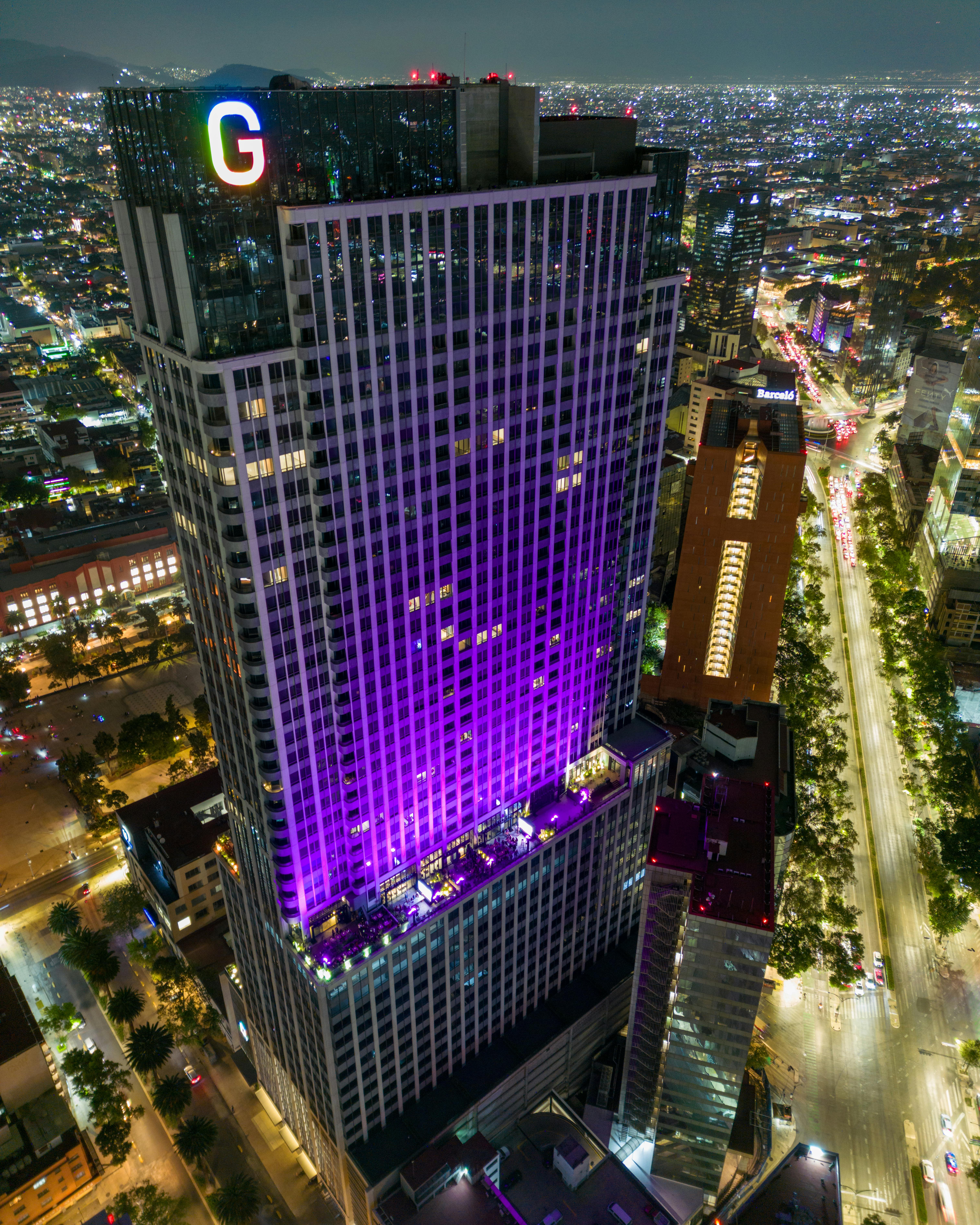 Stunning aerial shot of a brightly lit skyscraper in Mexico City at night, showcasing urban architecture and vibrant city life.