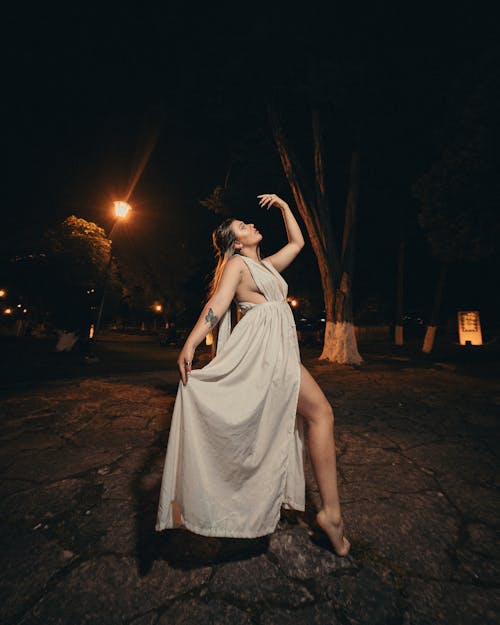 Woman in a Dress Posing Barefoot on a Street at Night 
