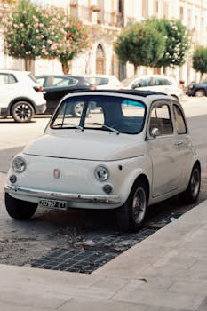 Vintage white Fiat 500 parked on a sunny street in Syracuse, Sicily, Italy.
