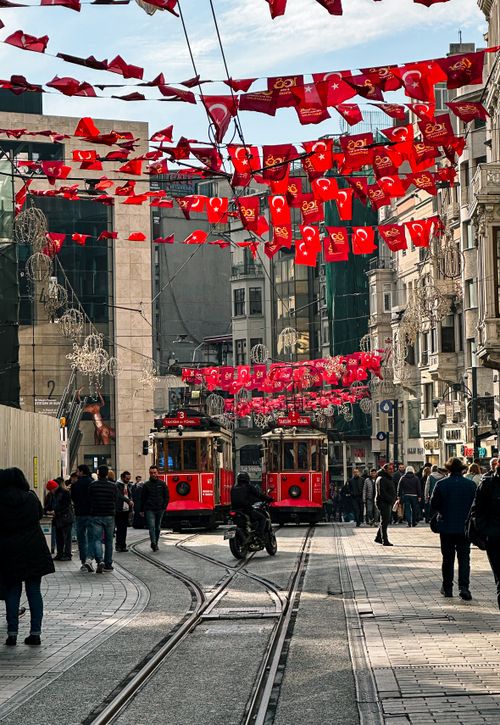 Free Lively street scene in Istanbul with red trams and Turkish flags, capturing the city's dynamic urban life. Stock Photo