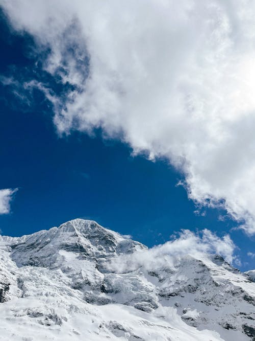 View of a Snowy Mountain Peak under Blue Sky with White Clouds 