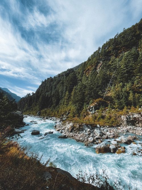 Free A picturesque river winds through a lush forested valley, framed by mountains and a vivid sky. Stock Photo