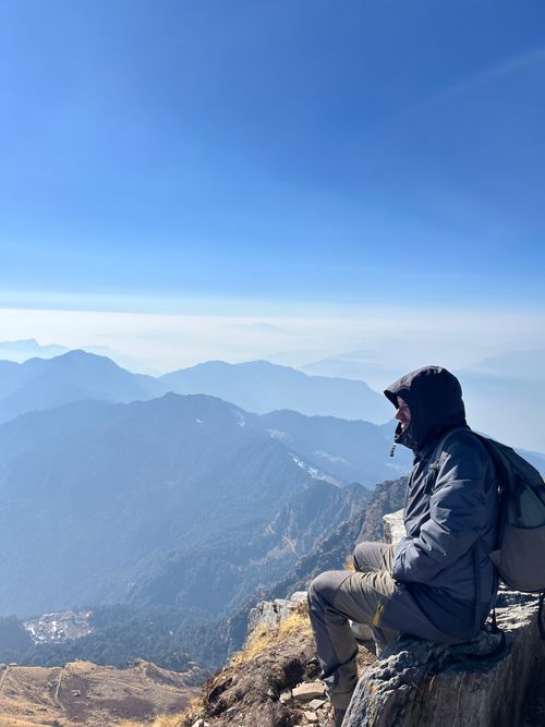 Free A man sitting on a mountain peak, enjoying the vast scenic view under a clear blue sky. Stock Photo