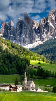 Stunning view of a church in Val di Funes with the dramatic Dolomites mountains towering above.