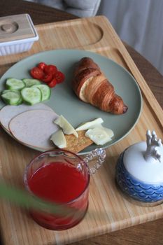 A breakfast tray featuring a croissant, sliced vegetables, and a refreshing glass of juice.
