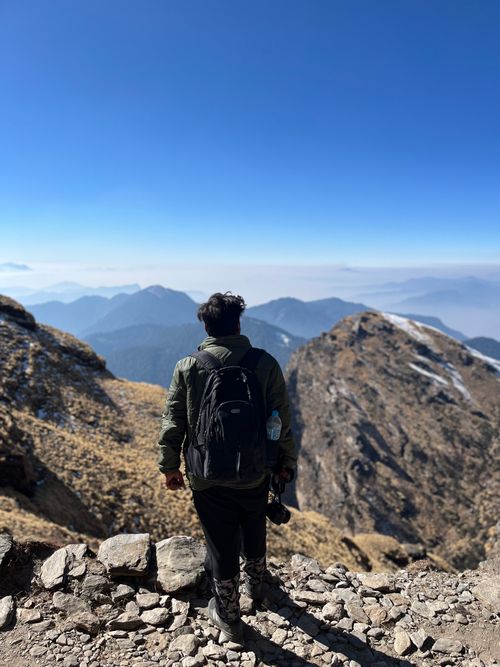 Free Man with backpack on a rocky mountain trail with scenic valley view. Stock Photo