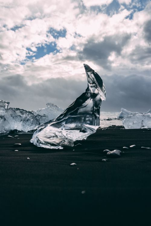 Free A striking iceberg on black sand with dramatic clouds in the background. Stock Photo