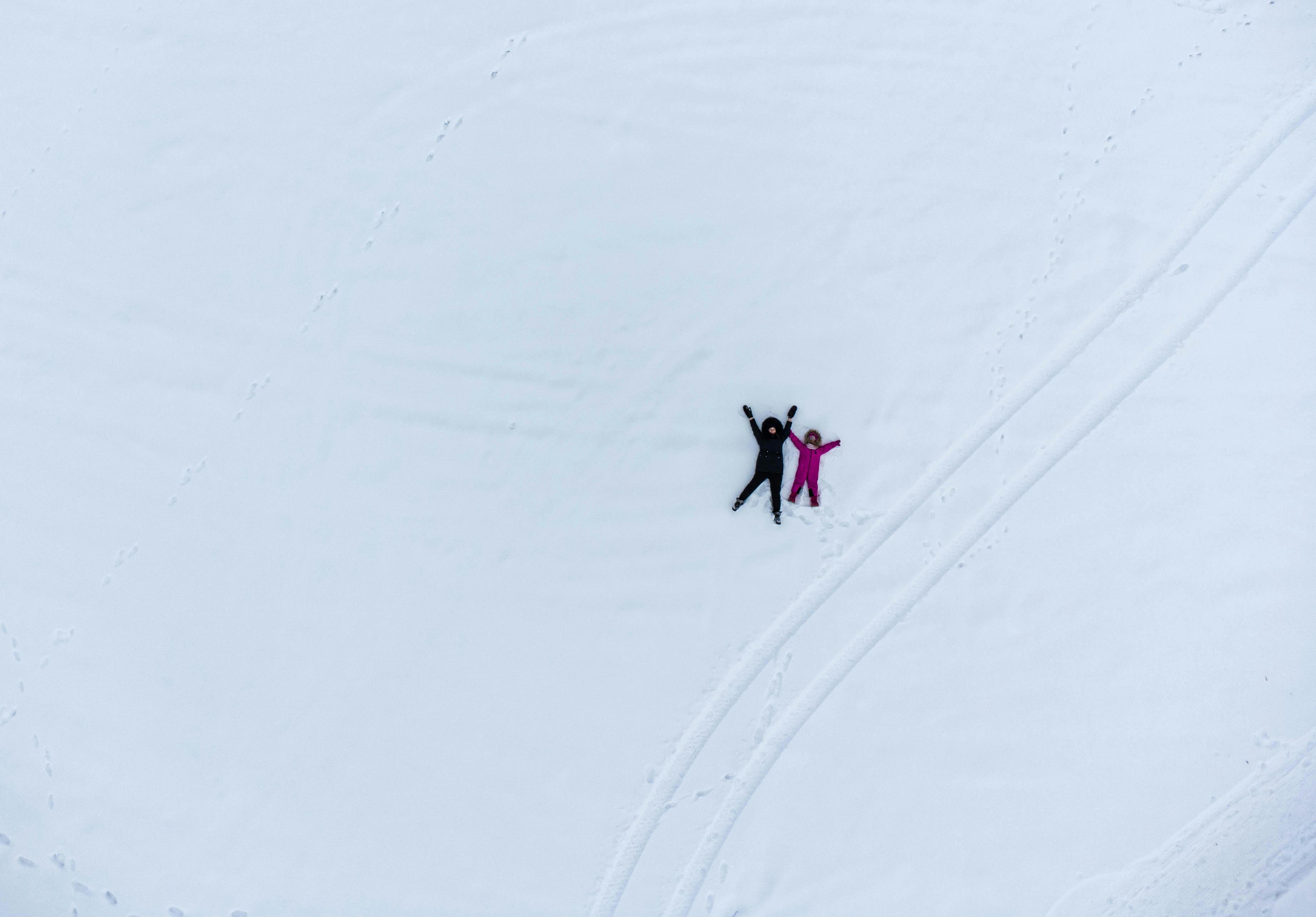 Aerial shot of two people lying in snow making snow angels, enjoying a winter day outdoors.