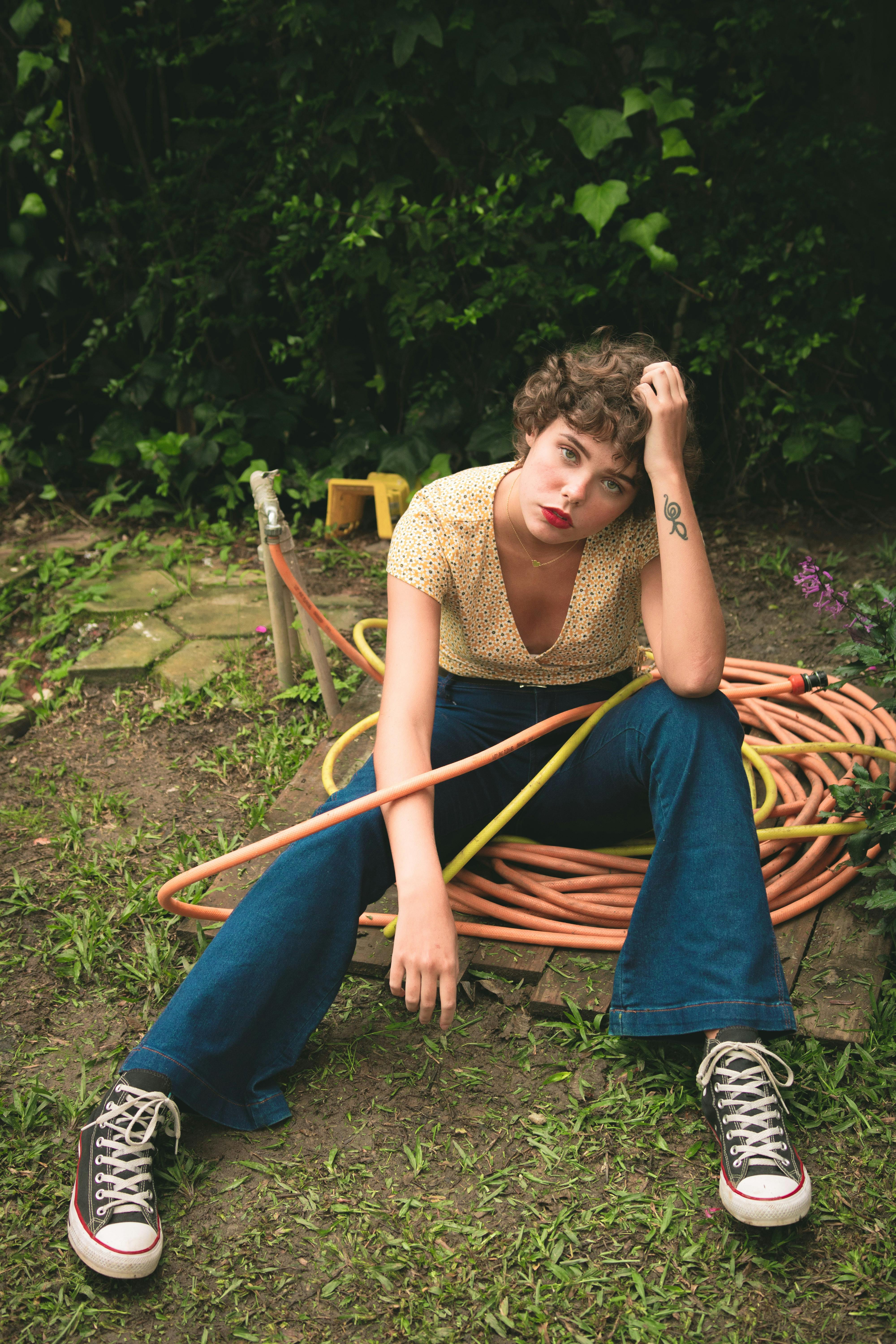 A relaxed young woman posing with a garden hose, embodying a casual summer vibe.
