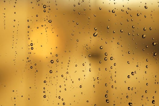Close-up of raindrops on a glass window with a warm yellow background creating an abstract pattern.
