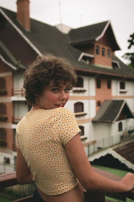 A young woman with curly hair smiling and posing by a stylish building in daylight.