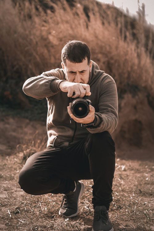 Free A photographer in a hoodie crouches outdoors in rural Algeria, capturing a scene. Stock Photo
