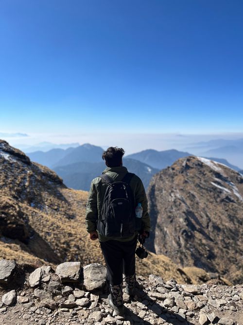 Free Man with backpack on scenic mountain trail overlooking picturesque valley under clear blue sky. Stock Photo