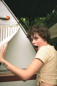 Young woman with curly hair exploring a camper van, showing excitement outdoors.