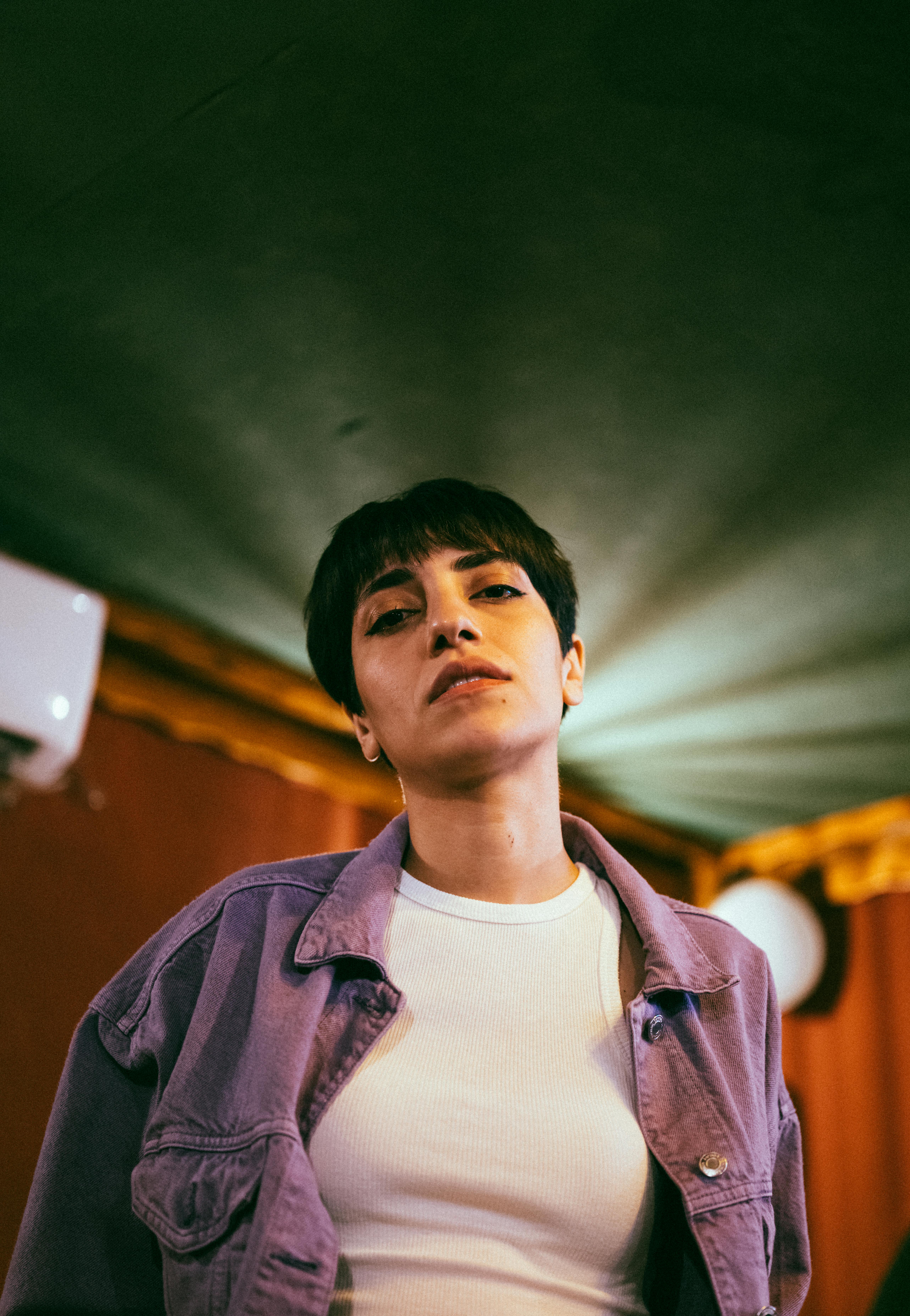 Portrait of a stylish woman with short black hair in a purple jacket, indoor setting.