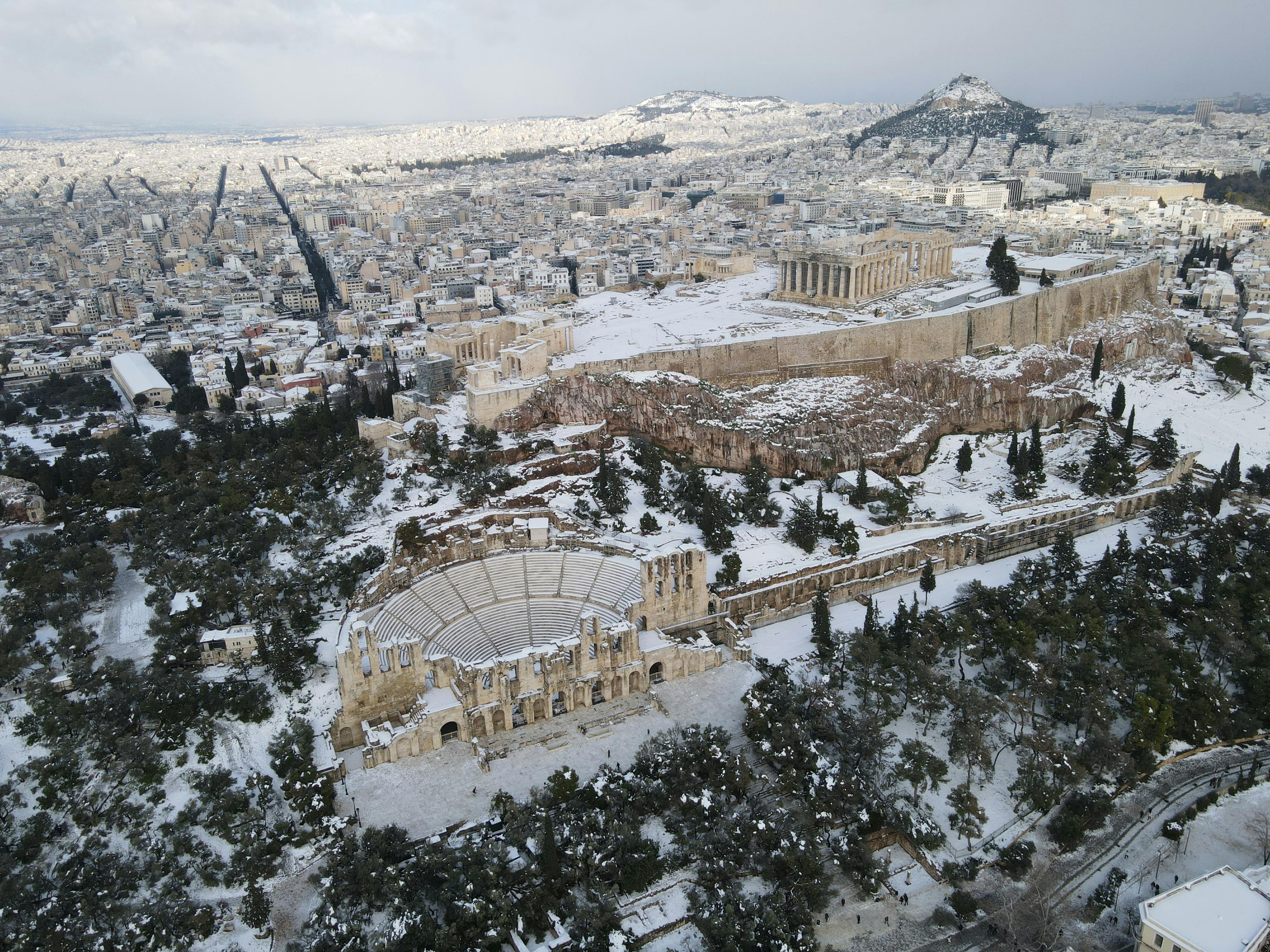 Aerial view of a snow-covered Acropolis in Athens, showcasing the ancient theater and landmarks.