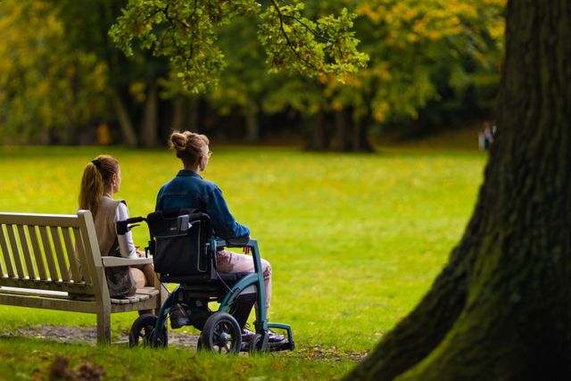 Duas mulheres convivendo no parque, uma delas em cadeira de rodas.