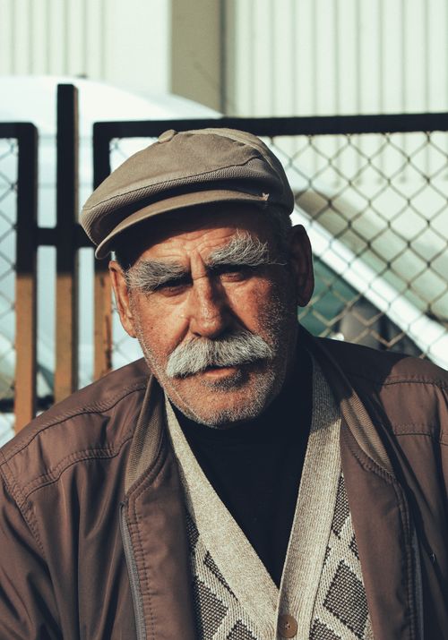 Free Portrait of an elderly man with a cap and moustache outdoors. Captures wisdom and character. Stock Photo