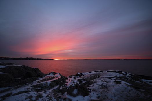 Gorgeous sunset over snowy rocks by the sea, capturing winter beauty.