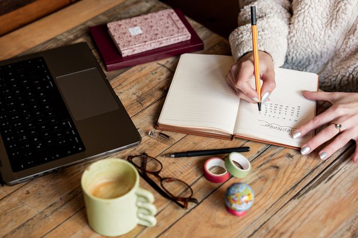 A planner and notebook on a desk beside a laptop and coffee