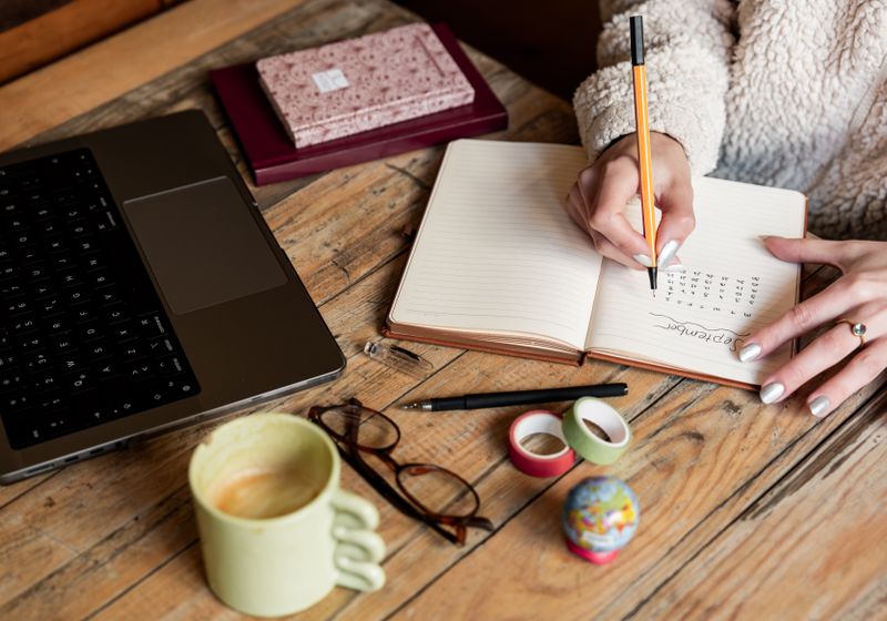 A desk with an open planner, pencil, coffee cup and laptop in warm light