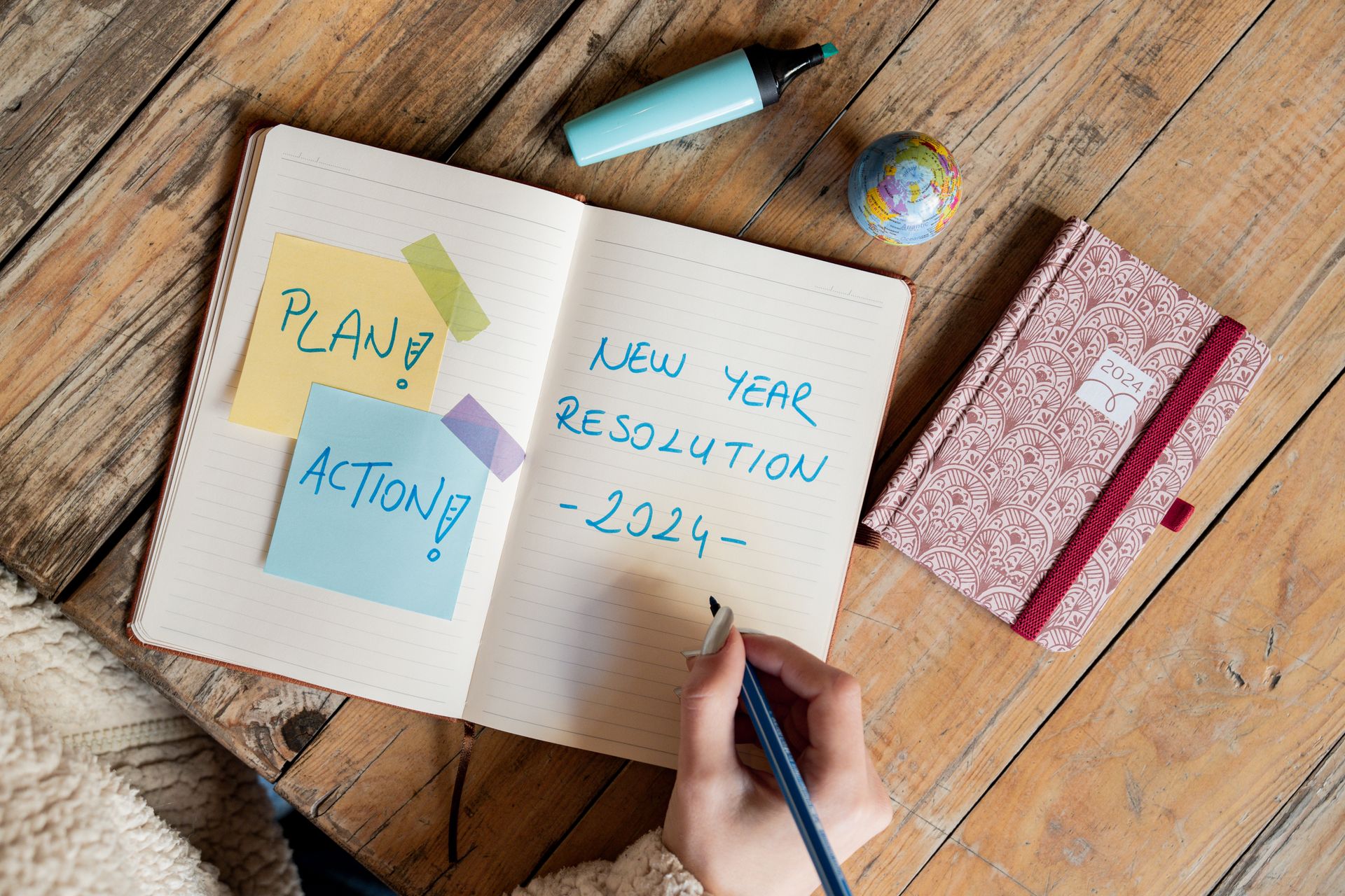 Person writing New Year resolution in a notebook with a pen, symbolizing goal setting for 2024.