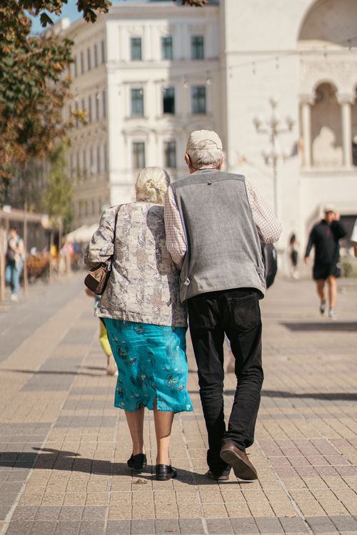 Free Senior couple strolling arm in arm on a sunny city day, capturing life's quiet moments. Stock Photo