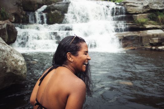 Joyful moment captured as a woman enjoys a refreshing waterfall in nature.