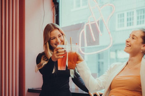 Friends Sitting by the Window of a Cafe with a Neon Finger Heart Gesture