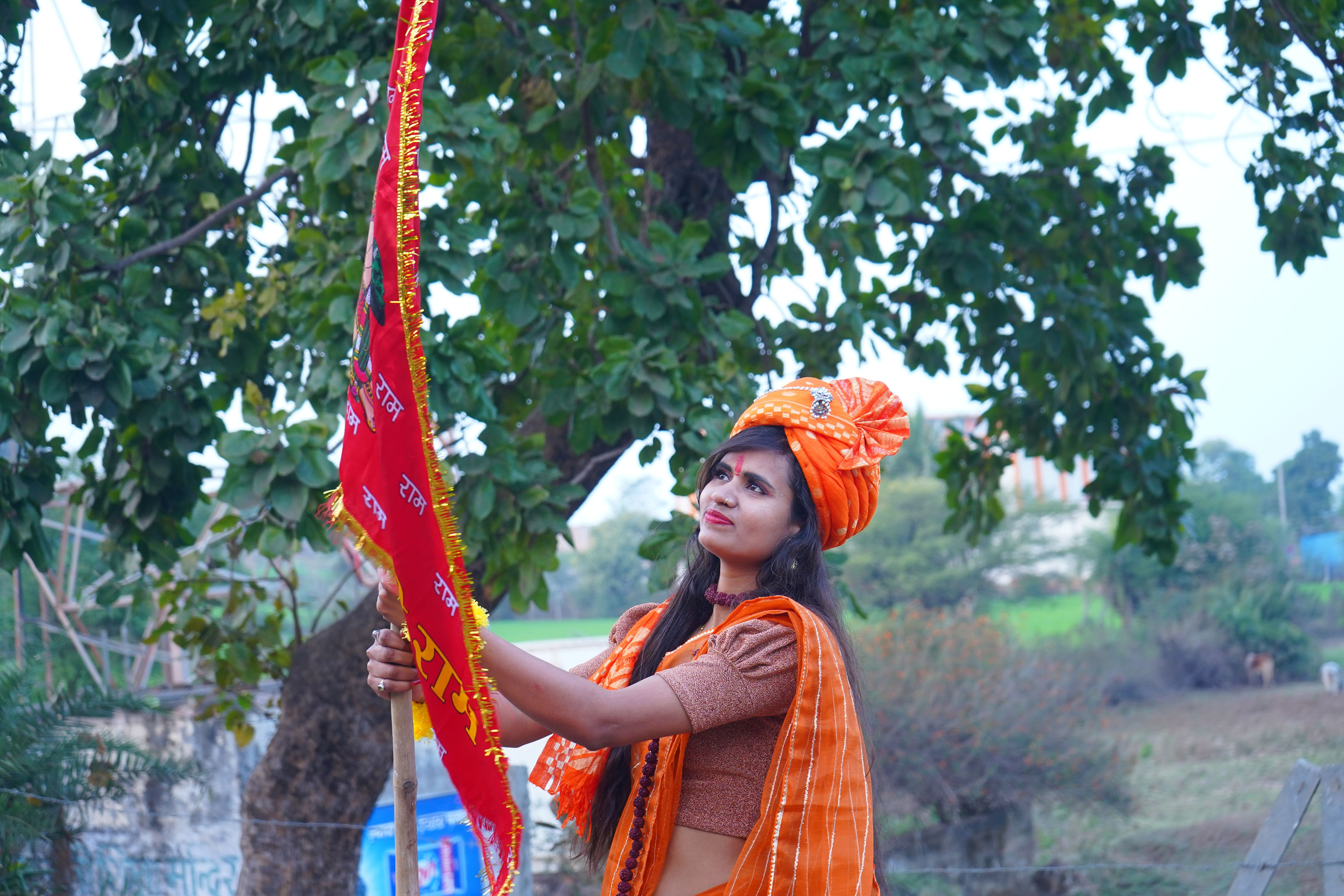 A woman in traditional Indian attire holding a decorative flag outdoors.