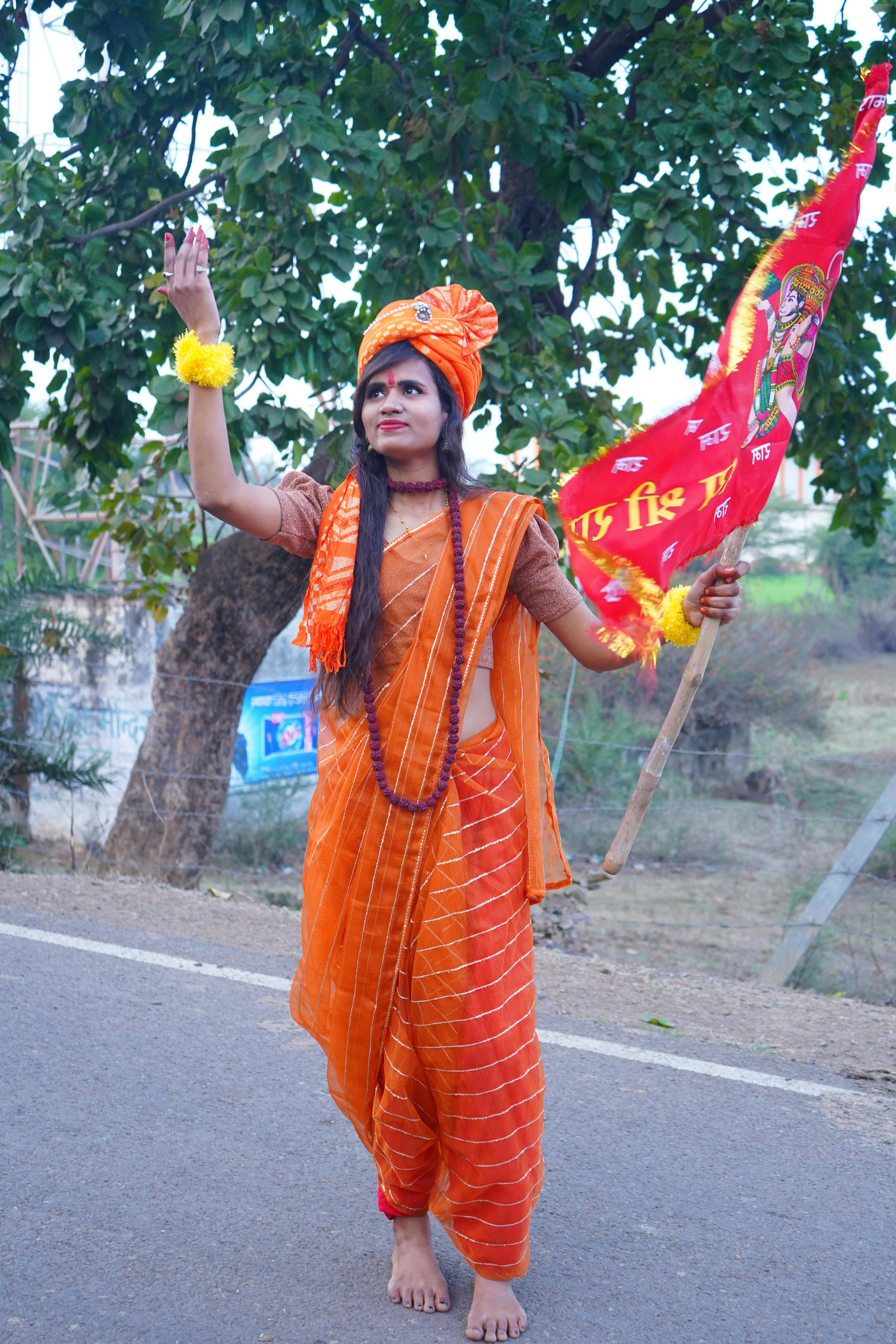 A South Asian woman in traditional attire holding a flag, celebrating outdoors.
