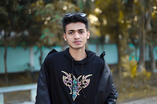 Fashionable young man in a black hoodie posing outdoors surrounded by nature.