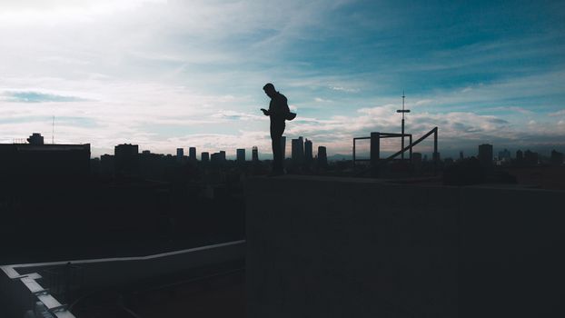 Silhouette of a man standing on a rooftop edge overlooking the skyline of Mexico City at daytime.