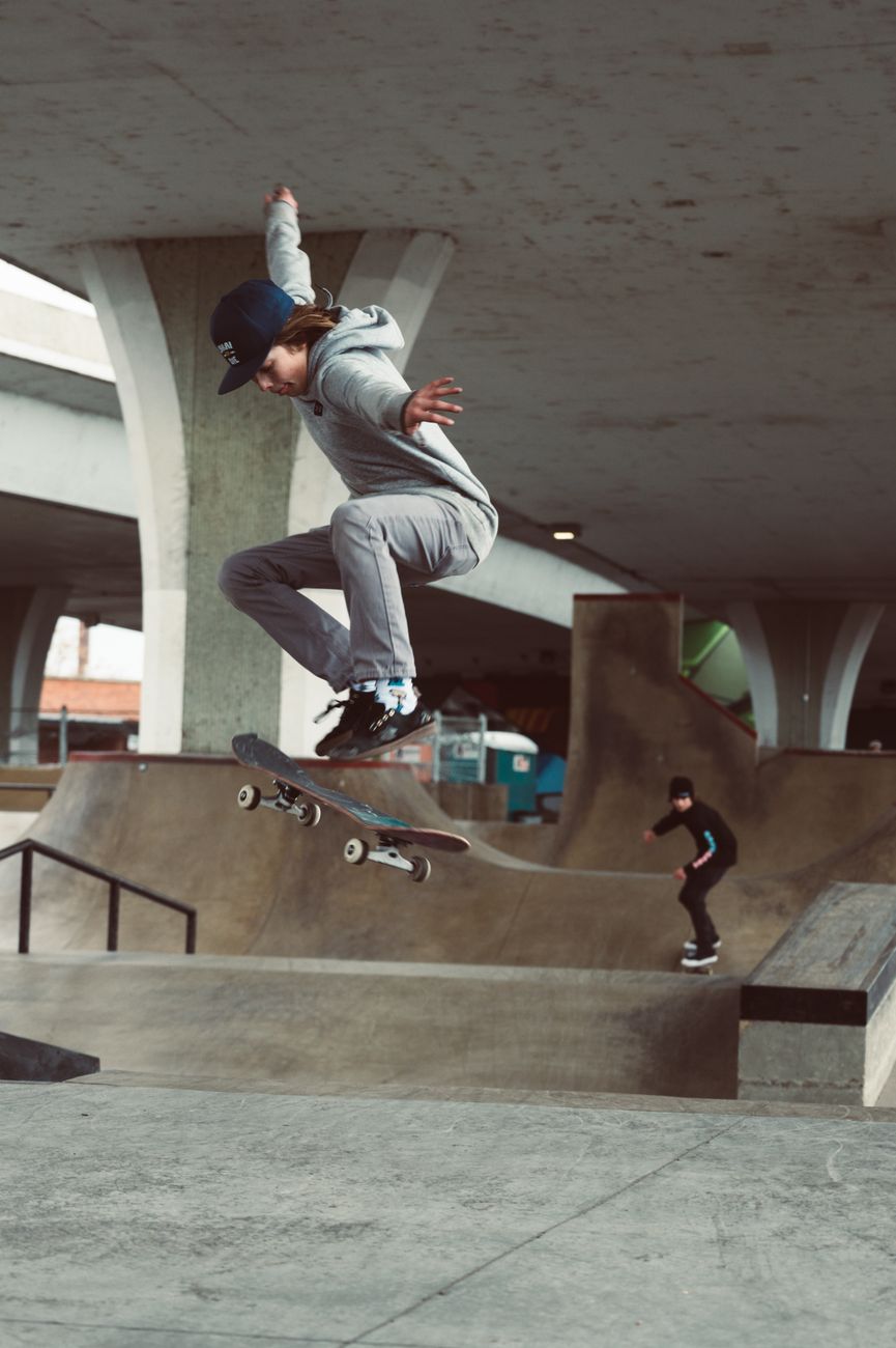 Skater performing a trick mid-air at an urban city skatepark beneath a concrete overpass.. skater, performing, trick