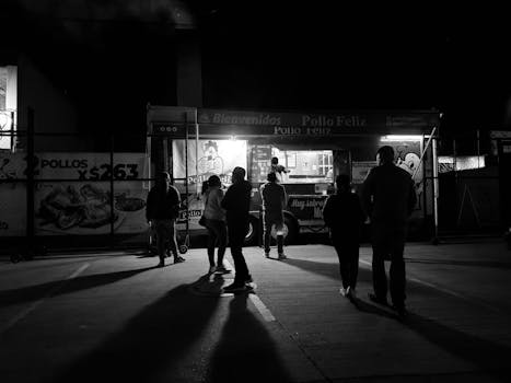 People gather at a food truck at night in a monochrome urban setting.