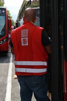 Back view of a traffic worker in red vest managing city buses during daytime.
