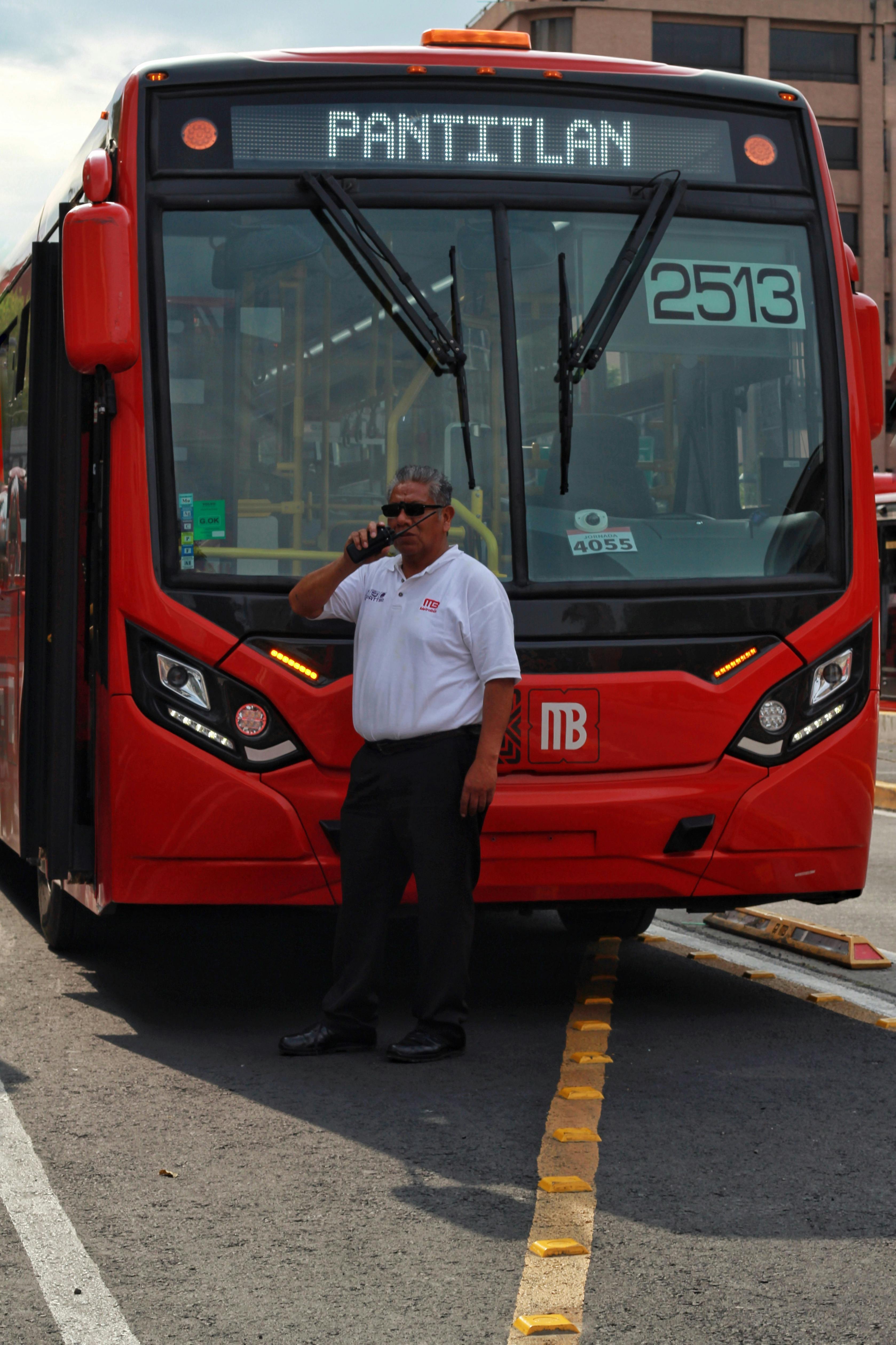 Free A bus driver stands beside a city bus at a bustling urban station. Stock Photo