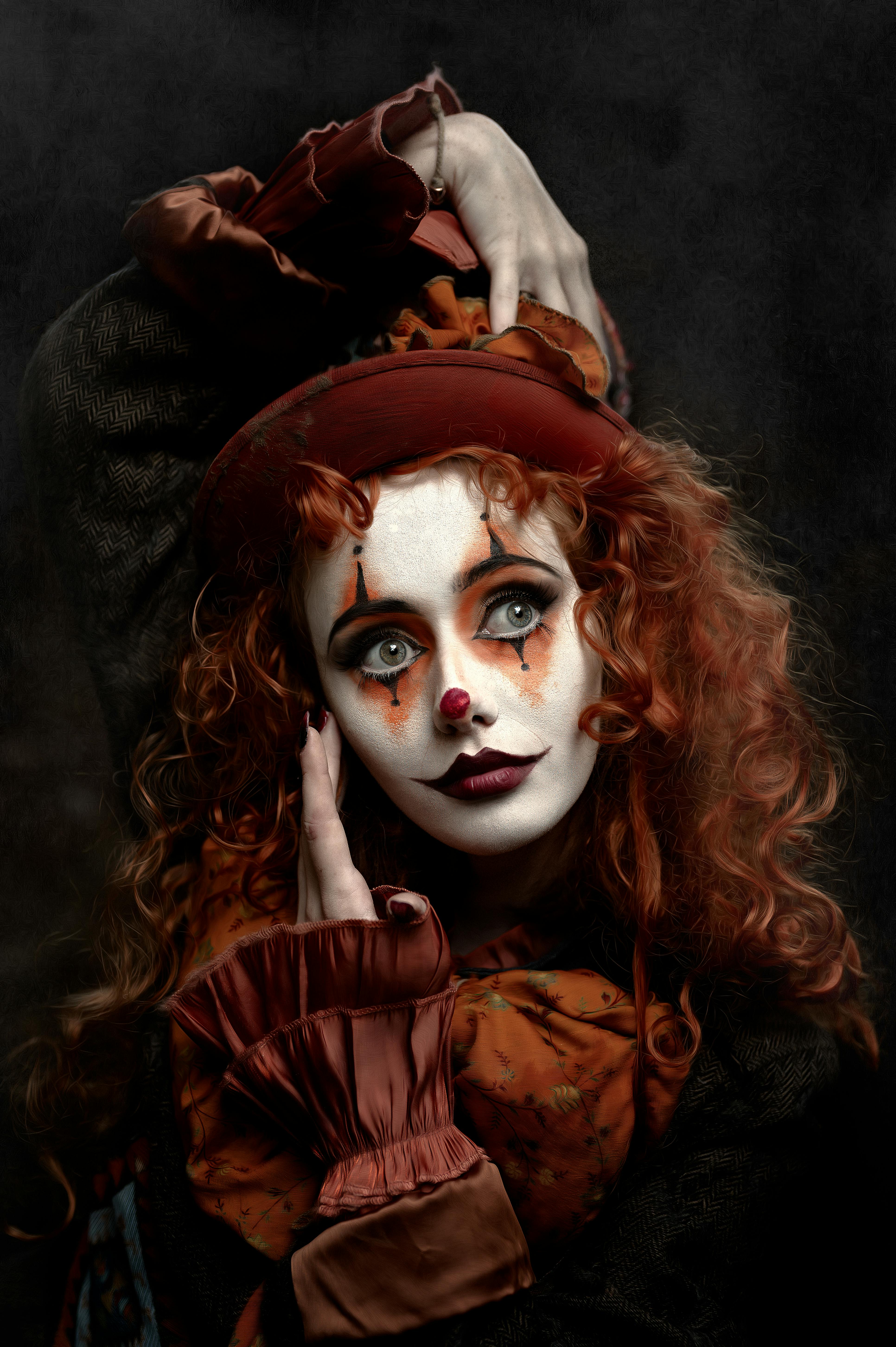 Free A striking portrait of a redhead woman in clown makeup posing with a vintage dress on a dark background. Stock Photo