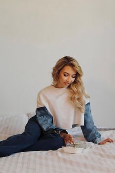 Stylish woman in casual wear sitting on a bed with relaxed demeanor.